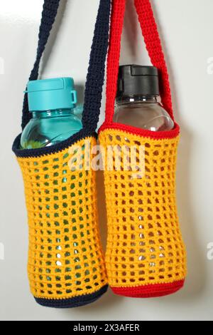Knitted red, yellow and blue drinking water bottle holder isolated on white background. Stock Photo