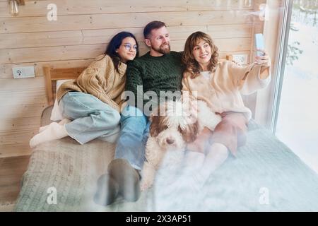 High angle view of modern Caucasian family with dog relaxing on bed at home taking selfies on smartphone, copy space Stock Photo