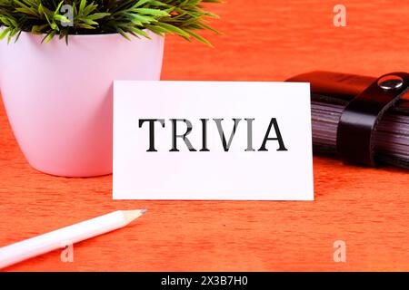 TRIVIA word it is written on a white business card next to a business card holder, pencil and plants in a white pot Stock Photo