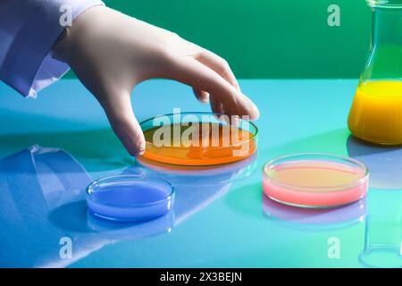 Female scientist is about to pick up the petri dish filled with chemical liquid in orange color. Experiments containing chemical liquid in laboratory Stock Photo
