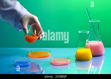 Liquid purification in the laboratory with a scientist holding a beaker containing orange chemical to pour into a glass petri dish. Conical flasks and Stock Photo