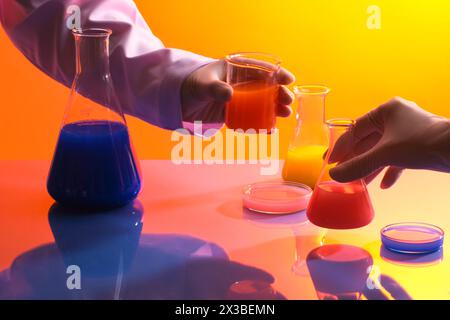 Professional scientists are holding a beaker and a conical flask filled with orange liquid. Chemistry lab laboratory technical equipment with many gla Stock Photo