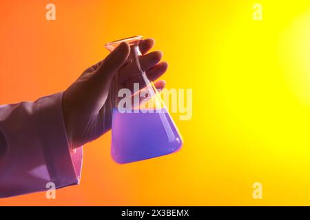 Minimal scene of a female scientist with medical glove holding a beaker containing purple liquid. Gradient background. Medicine experiment and chemica Stock Photo