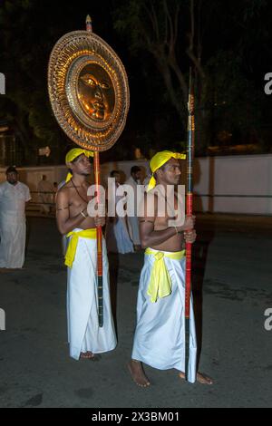 A Spear Carrier walks ahead of a Gilded Sun Disc Carrier along a street at Kandy in Sri Lanka during the Esala Perahera (great procession). Stock Photo
