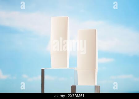 Blank label tube in white color placed on glass podiums over the blue sky background. Mockup for your design. Beauty products for moisturizing and ski Stock Photo