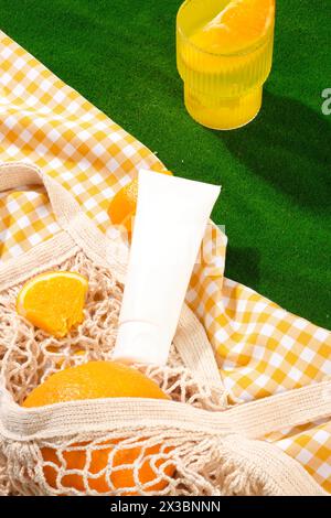 White and orange checkered fabric with a mesh bag containing oranges placed on. Unbranded tube in white color for branding mockup. The concept of suns Stock Photo