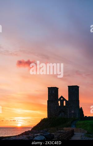 Sunset over the sea at the ruined twin towers of the the Anglo-Saxon church at Reculver on the Kent coast near Herne Bay. Towers are almost in silhouette against a bright yellow and red pink sky. Stock Photo