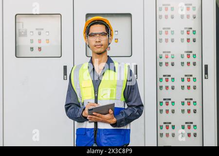 Asian male electrician engineer works standing at main circuit cabinet switchboard control water cooling pumping supply system. Stock Photo
