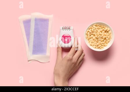Female hand with modern epilator, wax and strips on pink background Stock Photo