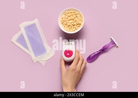 Female hand with modern epilator, wax and razor on lilac background Stock Photo