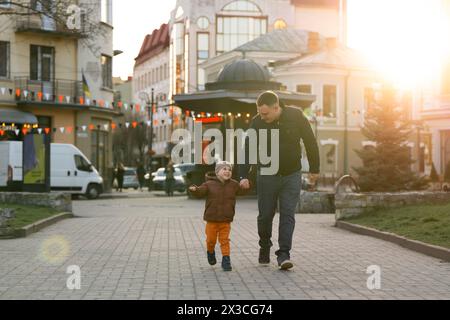 A happy three year old son walks hand in hand with his dad in the city on a sunny spring day. Family fun time and leisure. Spending time Stock Photo