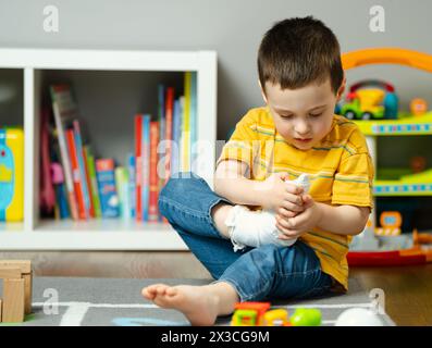 A little toddler boy holds his leg in a cast with his hands. Fracture of a foot and finger in children. Human healthcare and medicine concept. Bandage Stock Photo