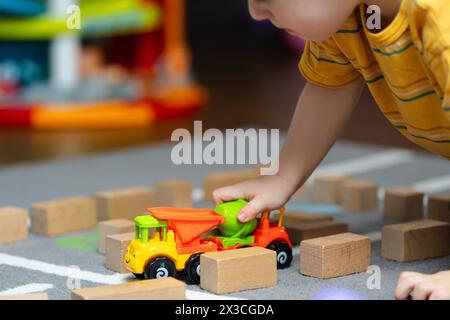 Toddler boy playing with a toy and wooden blocks on the floor in the children's room. Children leisure and lifestyle. Childhood. Focus on the little c Stock Photo