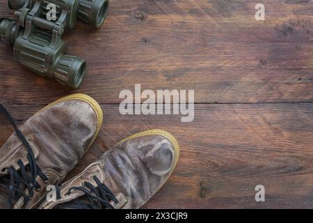 Binoculars and old trekking boots from brown leather on dark rustic wood, travel concept for a hiking adventure, high angle view from above, copy spac Stock Photo