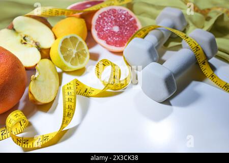 Fresh citrus fruits, apples, measuring tape and dumbbells, concept for a healthy lifestyle with fitness, sports and vitamin rich foods, light gray bac Stock Photo