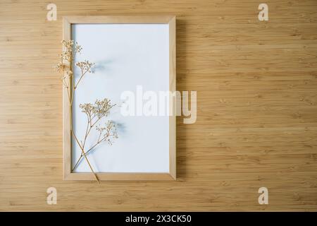 Small twig of gypsophila on an empty picture frame on a bamboo background, still life and home decor in minimalist Japandi style, background for produ Stock Photo