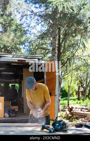 Caucasian man sanding wood to camperize his camper van outdoors Stock Photo