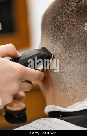 Barber uses clipper on mans hair, near forehead, ear, chin, temple Stock Photo