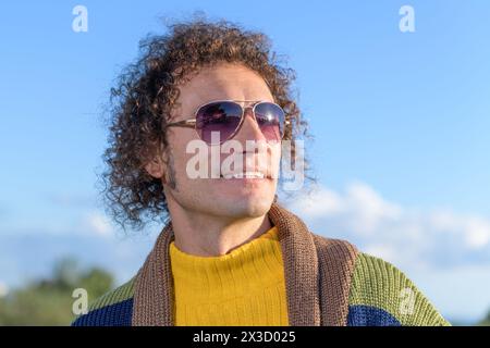 A happy curly-haired man in sunglasses is smiling, close up portrait Stock Photo