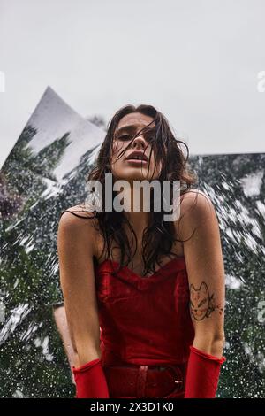 A mesmerizing scene unfolds as a young woman in a striking red dress and long gloves stands gracefully against a backdrop of a mountain. Stock Photo