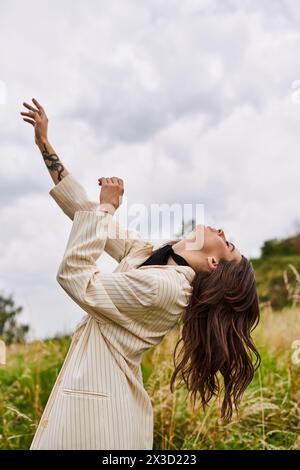 A beautiful young woman in white attire standing gracefully in a field of tall grass, feeling the summer breeze. Stock Photo