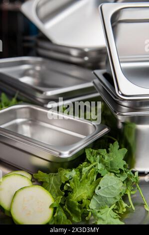Professional kitchen with stacked stainless steel pans and greens Stock Photo