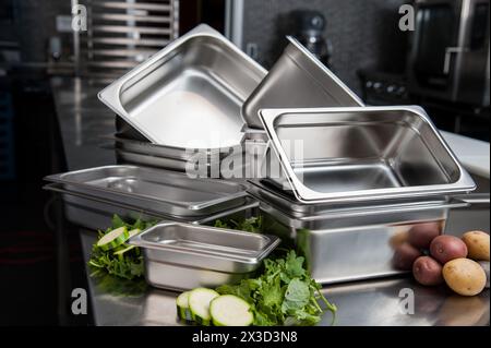 Stacked stainless steel pans and fresh vegetables on prep table Stock Photo