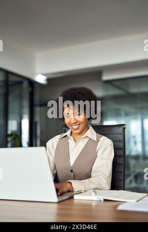 Young happy African American female employee using laptop working in office. Stock Photo