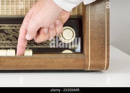 A real radio from the 60s. A man's hand turns on the button. Close-up plan. On a white background. Traces of time. Stock Photo