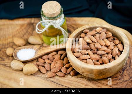Almond (Prunus dulcis, Prunus amygdalus, Amygdalus communis, Amygdalus dulcis), salted almonds in a wooden bowl with uncracked almonds, spoon with sal Stock Photo