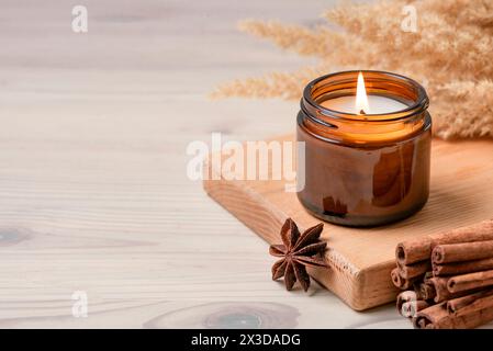 Massage scented burning candle in amber glass jar, winter hygge home interior decor on wooden table with cinnamon sticks and anise, copy space. Soy wa Stock Photo
