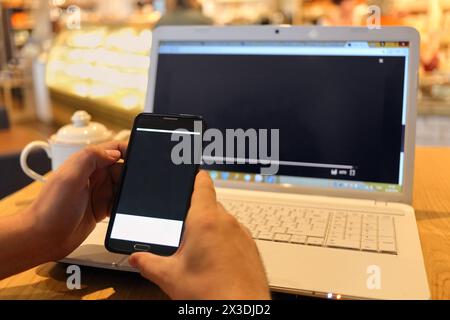 mans hands holding cell telephone and laptop on table in cafe, closeup Stock Photo