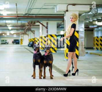 MOSCOW - JUN 01, 2015: Woman (with model release) with long hair in dress with two Doberman on leashes in the underground parking Stock Photo