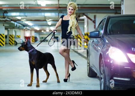MOSCOW - JUN 01, 2015: Blonde (with model release) with long hair in dress with the Doberman on leash in the underground parking Stock Photo