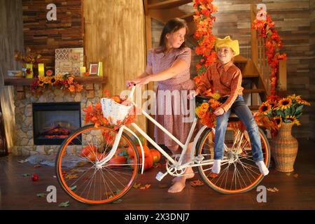 Mother is carrying her daughter on a bicycle in front of a fireplace and stairs in the room Stock Photo