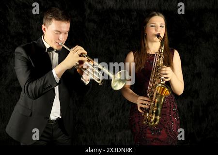 Two jazz musicians playing on wind instruments in a black room Stock Photo