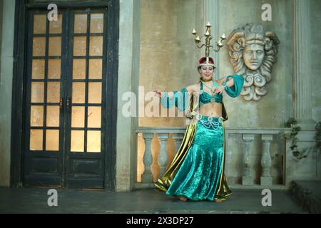 Beautiful woman in a green dress decorated with pearls and chandelier on her head performs Arabic dance Stock Photo