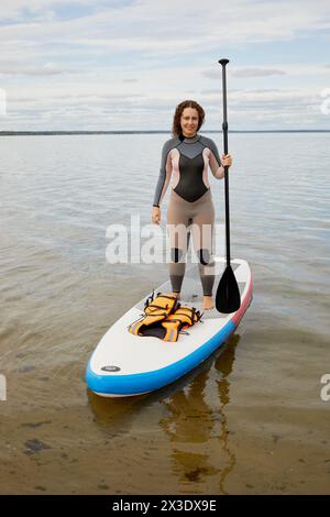 Woman in suit stands with paddle in hand on inflatable SUP board. Stock Photo