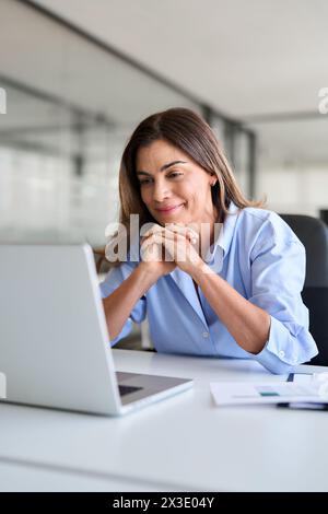Happy business woman of middle age looking at laptop working in office. Vertical Stock Photo