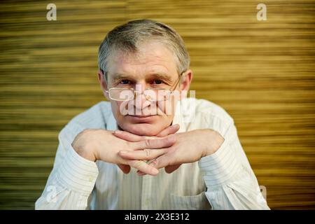 Portrait of smiling elderly grey-haired man in glasses, propping chin with folded hands. Stock Photo