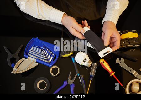 Male hands hold black tube above table with different tools. Stock Photo