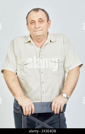 Portrait of elderly man standing propping hands on back of chair. Stock Photo