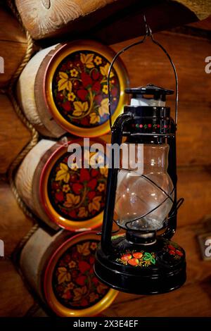 Old hanging gasoline lantern painted in Khokhloma style against wall of timber logs. Stock Photo