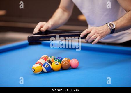Pool balls set arranged as triangle on blue billiard table and male hands lifting wooden rack. Stock Photo