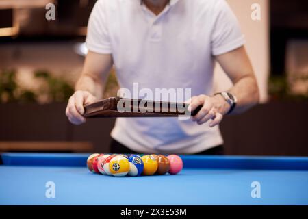 Man in white shirt arranges pool balls on table in club. Stock Photo