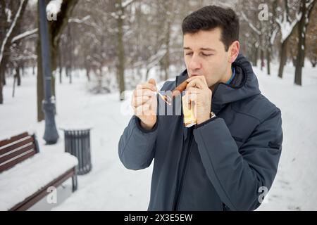 Man puffs at cigar in winter snowy park. Stock Photo