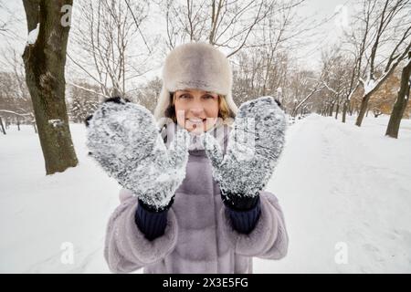 Smiling woman shows mittens with stuck snow in winter park. Stock Photo