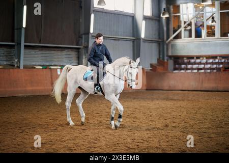 Man sits on horseback at covered riding arena. Stock Photo