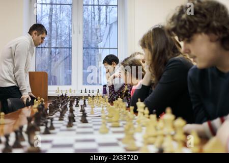 Six people (adults and children) play chess on table in chess club Stock Photo