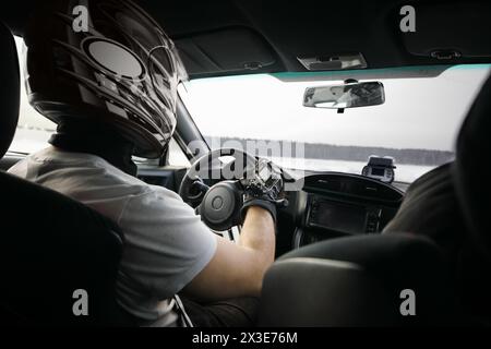 Racer in black helmet drives modern sport car with action camera on hand during competition at winter Stock Photo